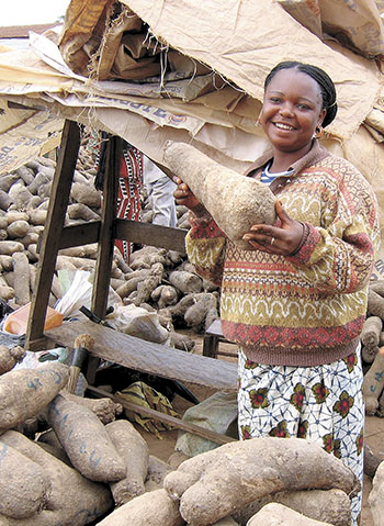 A woman holds up a giant yam at a market in the Igbo territory of Nigeria. (PHOTO COURTESY OF KP STUDIOS AND HARRIET KUHNLEIN)