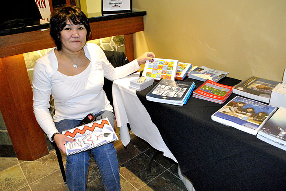 Aseena Allurut of the Nunavut Literacy Council displays a large collection of Inuit language materials that the council has helped produce and gather to promote reading and literacy among young people. It's one of several such promotions on display this week at the Inuit language standardization symposium that started Feb. 7 at the Frobisher Inn in Iqaluit. Many other projects are on display inside the hotel's Kitikmeot room. (PHOTO BY JIM BELL)