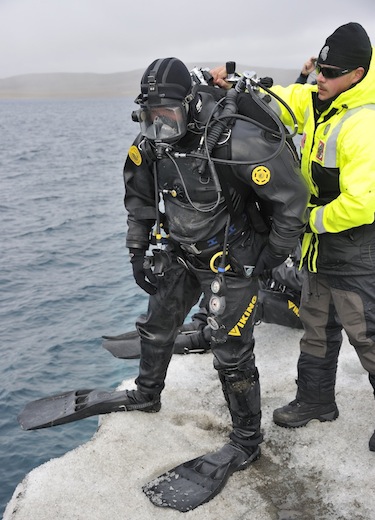 Petty Officer First Class William Roberts, with the United States Coast Guard, helps a fellow American Coast Guard diver prepare to enter the waters off of an iceberg that is being used as a diving platform during Op Nanook. (PHOTO BY SGT. NORM MCLEAN/CANADIAN FORCES COMBAT CAMERA/DND)
