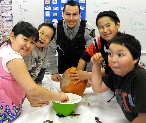 Volunteers, including RCMP Constable David Lawson (centre), health staff, hamlet and Canadian North, helped kids at Cape Dorset's Sam Pudlat School carve Halloween pumpkins last week. Children worked in small groups, demonstrating the schools Inuit Qaujimatuqaangit for that month, Pillriqatigiinniq or working together for a common cause, says teacher Emma Anso. Pumpkin-carvers also entered their names in an Oct. 28 draw to see who would to take their group's pumpkin home to display at home on Halloween night. (PHOTO COURTESY OF E. ANSO)