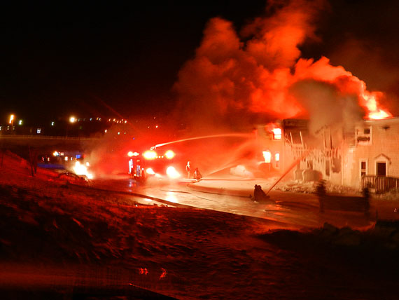 A big fire that began just after 10:00 p.m. Feb. 26 at rowhouse unit at the end of the 300-section of the Creekside Village complex in downtown Iqaluit was spreading through adjacent rowhouses by 11:30 p.m. that evening. Iqaluit firefighters were directing streams of water towards units at the back of the complex, while numerous residents looked on. Residents of the 300 block of rowhouses are asked to go to the lobby of the Frobisher Inn to hear more updates. Those who are unable to go there are asked to call the RCMP at 979-1111 to provide the RCMP with their location to ensure that all residents are accounted for. Most units in the affected section of the complex were occupied by Nunavut Arctic College students and their families, many of whom are now being offered accomodation at the Frobisher Inn. (PHOTO BY JIM BELL)