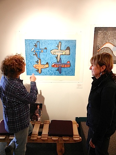 At the opening of the 2011 Pangnirtung Kyra Fisher (right) looks at Elisapee Ishulutaq’s print “International Formation: Two Canadians, one American & one German Fly the Arctic.” (IMAGE FROM THE 2011 PANG PRINT COLLECTION)
