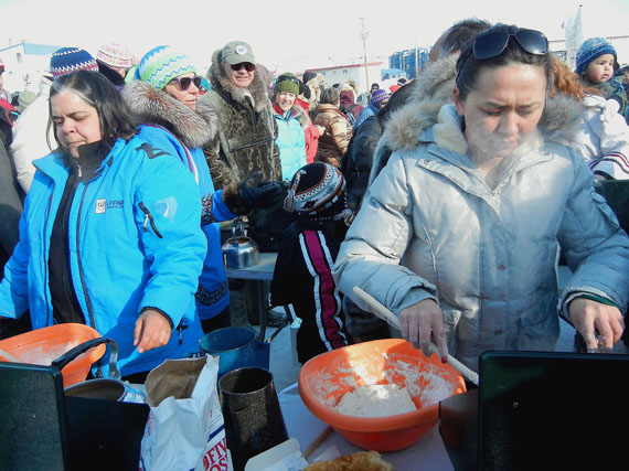 Two participants in the April 14 Toonik Tyme tea boiling and bannock making competition, held outside Iqaluit's Nakasuk elementary school, concentrate as they cook. (PHOTO BY JANE GEORGE)