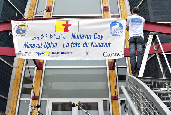 A volunteer hangs a Nunavut Day banner above the back entrance to the Nunavut legislative building in Iqaluit, at around 10:00 a.m., July 9. At 11:30 a.m. Nunavut Day festivities will kick off — rain or shine — at the legislative assembly parking lot. Iqaluit residents can look forward to country food, music, speeches, games and award presentations. (PHOTO BY JIM BELL)