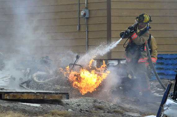An Iqaluit firefighter aims water at a snowmobile that caught fire around 7 p.m. May 15 behind house 1002 in the Lower Base neighbourhood of Iqaluit. The fire generated lots of smoke, lots of noise and many curious spectators. But firefighters brought it under control in about 25 minutes. (PHOTO BY JIM BELL)