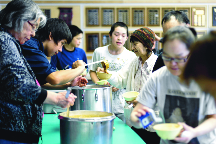 Volunteers Bessie Sitatak, far left, and Hikok Ivarluk, beside her, serve up bowls of caribou chili and char chowder Mar. 22 to Kugluktuk residents at a soup kitchen pilot project in the community's public library. The popular soup kitchen, which addresses some of the goals of Nunavut's food security strategy, ran every Saturday from January to March 2014 and organizers are hoping to find funding to get it up and running again. (PHOTO BY JESSE AJAYI)
