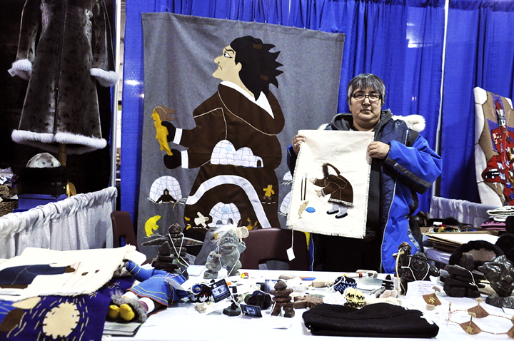 Kelly Putuguq of Goja Haven displays a wall hanging for sale at the Nattilik Heritage Society's booth during the 2014 Nunavut Trade Show & Conference in Iqaluit Oct. 9. The three-day event, which drew large crowds to the Arctic Winter Games Complex, wraps up Oct. 9. (PHOTO BY THOMAS ROHNER)