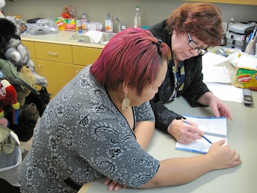 Trisha Ogina helps her fellow student Pam Langan, who both work at the May Hakongak library and cultural centre in Cambridge Bay, with her Inuinnaqtun language materials. (PHOTO BY JANE GEORGE)