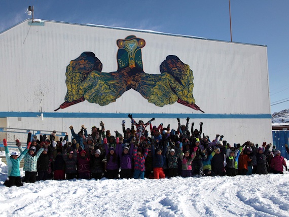 Students from Sam Pudlat Elementary School in Cape Dorset pose beneath a giant mural painted by local youth and installed on the school wall this past winter. Four young artists from the south Baffin community will be travelling to Toronto this summer to participate in a collaborative mural project. Read more later on Nunatsiaqonline.ca. (PHOTO COURTESY EMBASSY OF IMAGINATION)
