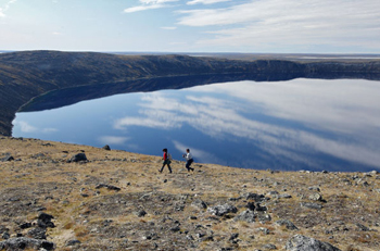 Two people walk along the shore of the Pingualuit crater, in the centre of the park of the same name. (PHOTO COURTESY OF PARKS NUNAVIK)