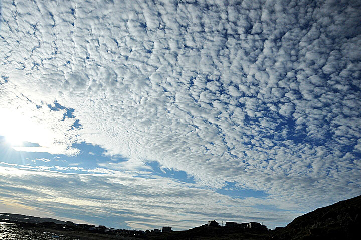 The sun descends behind a blanket of fluffy clouds over Iqaluit July 26, as seen from the Apex trail. These clouds, which give the sky a mottled texture, look like they might be altocumulus, or cirrocumulus. Iqalungmiut enjoyed a string of five sunny days between July 22 and July 26, when many people came outdoors to walk, socialize, camp, hunt and fish. Sadly, it looks like the sunny weather is about to end in Iqaluit. Environment Canada forecasts rain over the next seven days. (PHOTO BY THOMAS ROHNER)