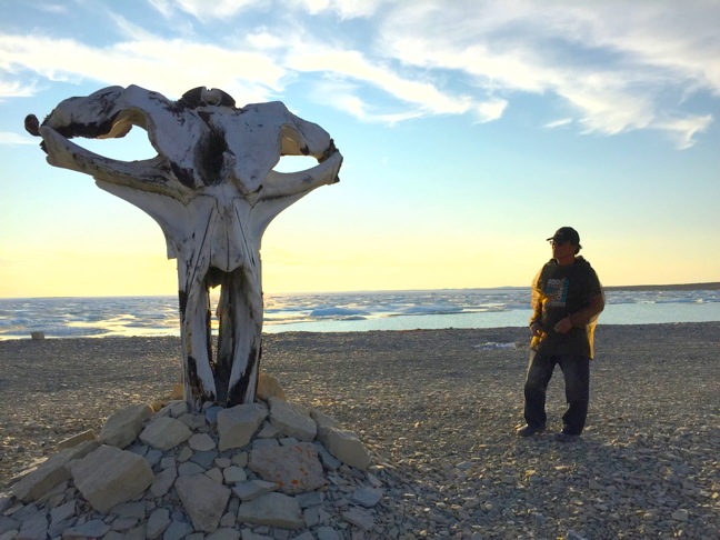 Igloolik filmmaker and hunter Zacharias Kunuk stands behind a bowhead skull that he and other locals recently erected on the shore of Ham Bay near Igloolik. (PHOTO BY GREGORY COYES/GOOD MEDICINE MEDIA)