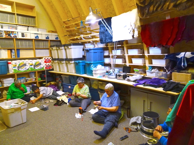 Elders at Cambridge Bay's May Hakongak library and cultural centre sew tiny pieces of sealskin for figures that will eventually end up on a large sealskin wall hanging. Shining from above is a flexible light bought purchased by Cambridge Bay resident Marg Epp, who donated the lamp to the cultural centre as a way of thanking the elders for their help.