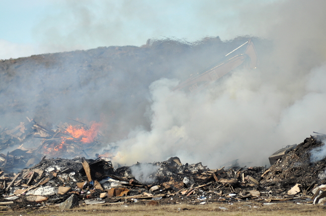 With waves of heat clearly visible in the upper half of this photo, city crews operating a barely visible excavator work to pull apart and suppress a fire in the scrap metal and wood section of the dump that began burning June 20. At least three pieces of heavy machinery, two water trucks and two municipal trucks are on scene as firefighters attempt to douse the fire which appears perilously close to the tank farm. The City of Iqaluit issued a news release to say residents are in no danger, but the fire is only about 200 metres from the nearest fuel tank. Smoke is currently blowing away from the city and into Sylvia Grinnell Territorial Park. The city advises that there will be no water delivery today and no commercial garbage pick-up today as city crews are assisting in firefighting efforts. Commercial garbage pick up will resume on the next scheduled day and water delivery is expected to resume tomorrow, June 22. (PHOTO BY THOMAS ROHNER)