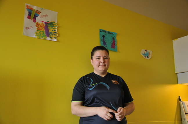 Erin Pameolik, 26, poses Sept. 8 beneath artwork made by her son and hung on the bright yellow walls of Pameolik's Nunavut Arctic College student residence in Iqaluit. Pameolik said she painted the wall herself after scrubbing the walls to remove the food stains, nose phlegm and filth that she found when she moved into a Q unit located behind Nunatta Campus in Iqaluit, before the start of the school year. (PHOTO BY THOMAS ROHNER)