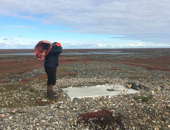 Tony Uluadluak visits the grave of his late father, Donald Uluadluak, located near Camp Lake, west of Arviat, Sept. 4. Fresh from a weekend hunt in the area, Uluadluak is hoisting ribs from a caribou his nephew caught earlier that day. (PHOTO COURTESY OF T. ULUADLUAK)