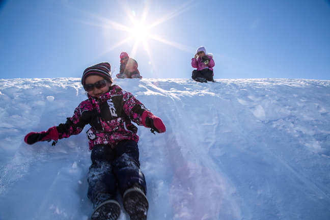 Joyce Kigutak, takes a trip downhill at Ikpikituarjak, one of the sites of this year's Arctic Bay fishing derbies held May 20. Lucy Kigutak, above left, and Marissa Qaqqasiq Taqtu, take a break in the brilliant sunshine before joining their friend. (PHOTO BY CLARE KINES)