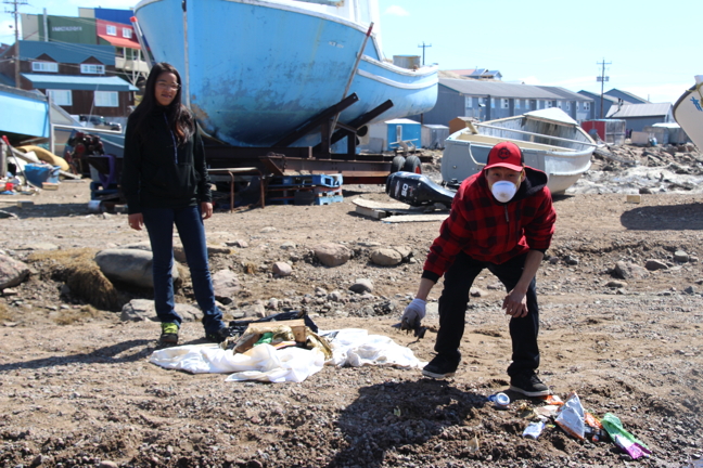 Tommy Kelly rolls up his sleeves to tidy up around some boats near the Iqaluit shoreline, with help from Sarah Mike.