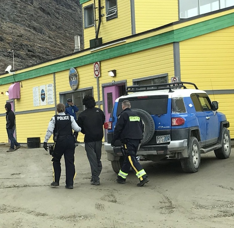 RCMP officers walk to the airport terminal with a man arrested in connection with a Sept. 15 fire in Pangnirtung. Since last month, the community of about 1,500 has seen about eight fires, which continue to be investigated by police. (PHOTO BY DANIEL KULUGUQTUQ)