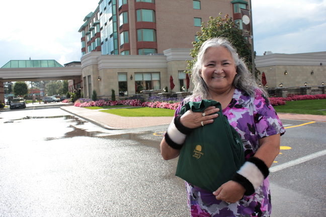Former Iqaluit mayor, and frequent Southway Inn patron, holds up her Southway Inn shirt in front of the old hotel, now a retirement residence at Bank Street and Hunt Club Road.
