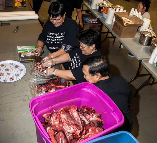 Canada 150 committee members (from bottom) Philip Kalluk, Piuyuq Enoogoo and Sarah Alooloo cut up tunnuk and tuktu in preparation for the community feast Nov. 15 in Arctic Bay.