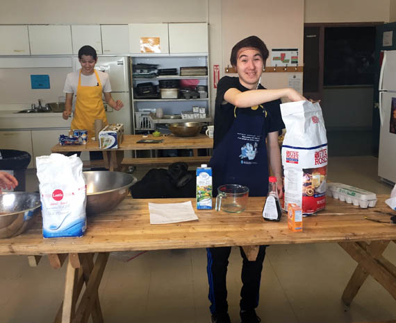 Tommy Annanack Lacasse, with his hand in a bag of flour, and Amaruq Rousseau behind him in a yellow apron, work at the Old Rock Café, based out of the kitchen at Innalik school in Inukjuak. (PHOTO COURTESY OF YOUTH FUSION)
