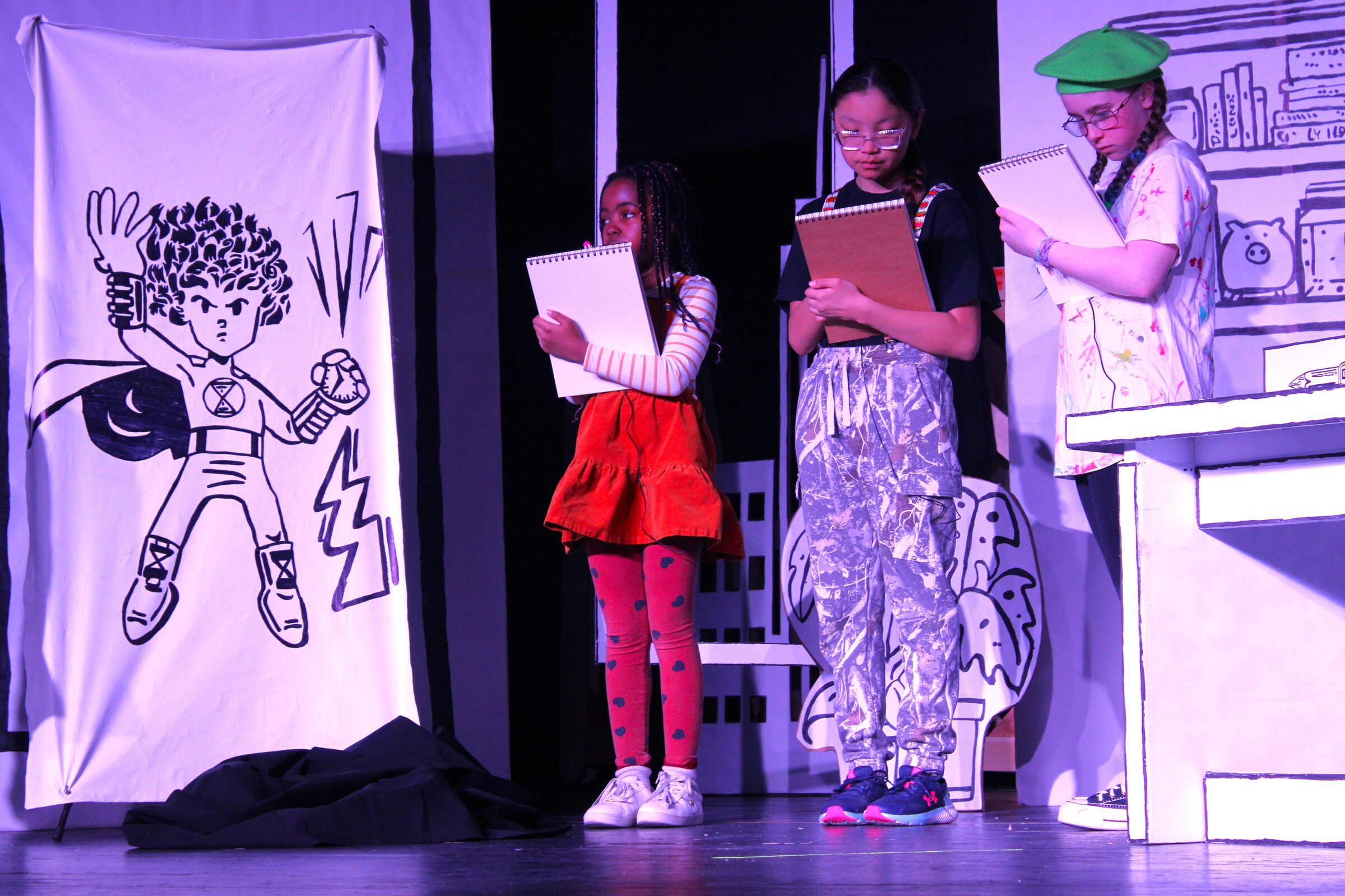 Elaine Poshai, left, Victoria Groves and Maisie MacDonald sketch comic book heroes that spring to life in “Adventures of a Comic Book Artist.” The musical play runs Friday at Nakasuk School in Iqaluit, rescheduled from Wednesday due to a blizzard. Admission is free and all are welcome. Doors open at 6 p.m. and the play starts at 6:30 p.m. (Photo by Daron Letts)