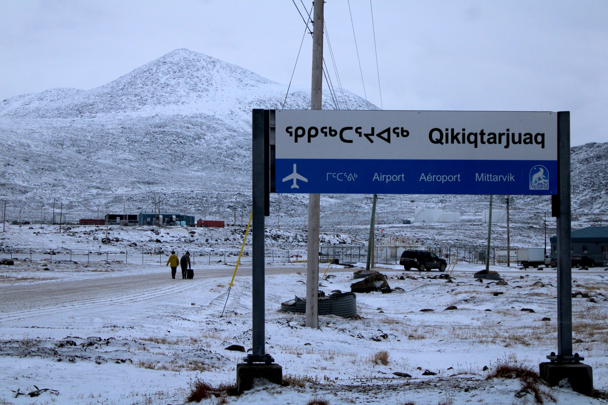 Two women wheel a suitcase through snow and gravel in 0 C temperatures on their way to the airport in Qikiqtarjuaq to catch an afternoon flight Monday. The airport is roughly a kilometre away from the hamlet’s core area. Like most smaller Nunavut communities, Qikiqtarjuaq does not have a taxi service. (Photo by Arty Sarkisian)