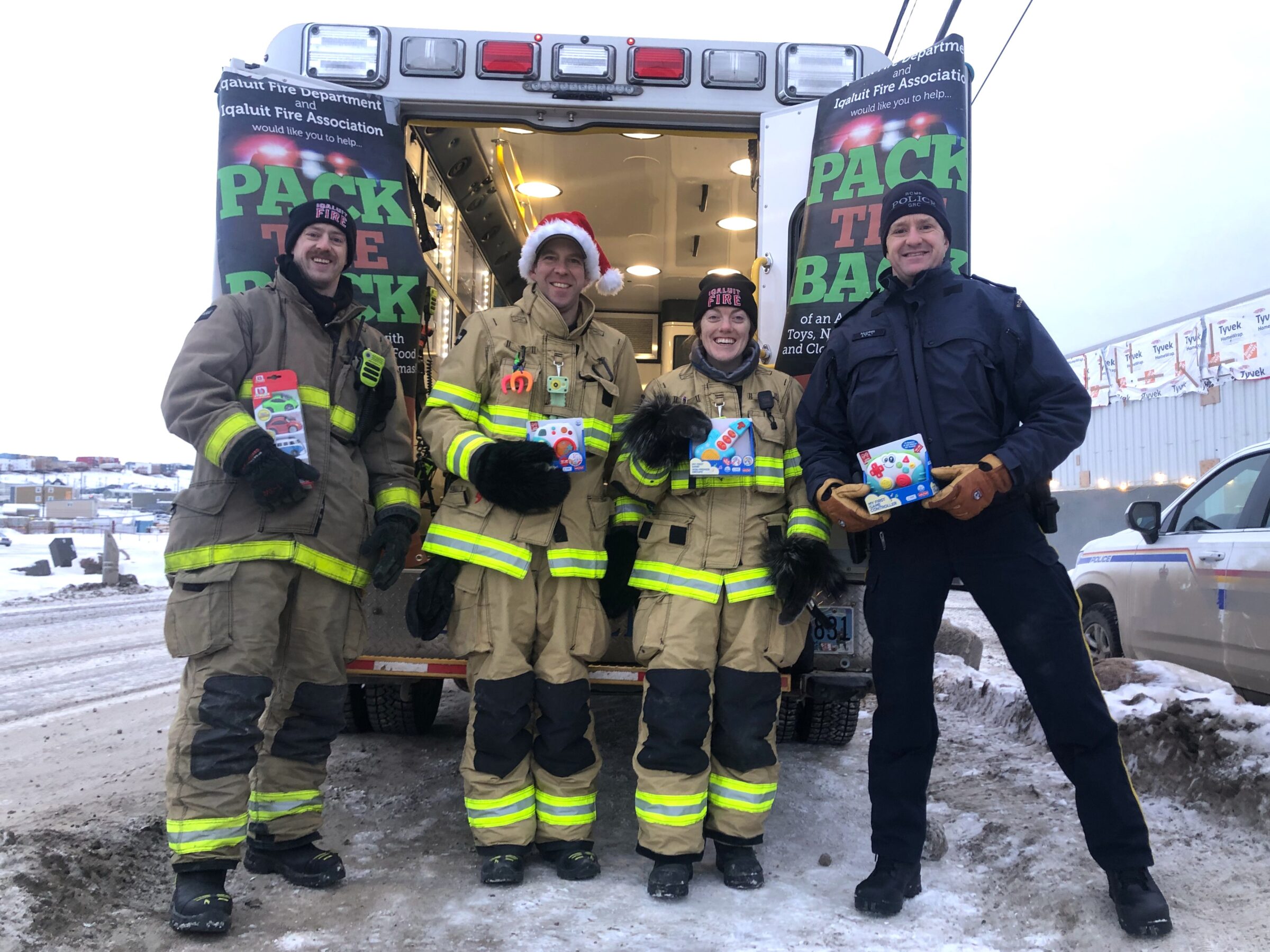 Iqaluit firefighters Matthew Crossman, left, Mitch Bacon and Taylor Clark, and RCMP Insp. Will McGinis accept their first donations of the day Saturday during the Pack the Back toy and food drive. The crew set up in front of Northmart first, then collected more donations at Arctic Ventures in the afternoon. They filled the ambulance with toys, food, and warm clothing and accepted $900 in cash and gift cards. (Photo by Daron Letts)