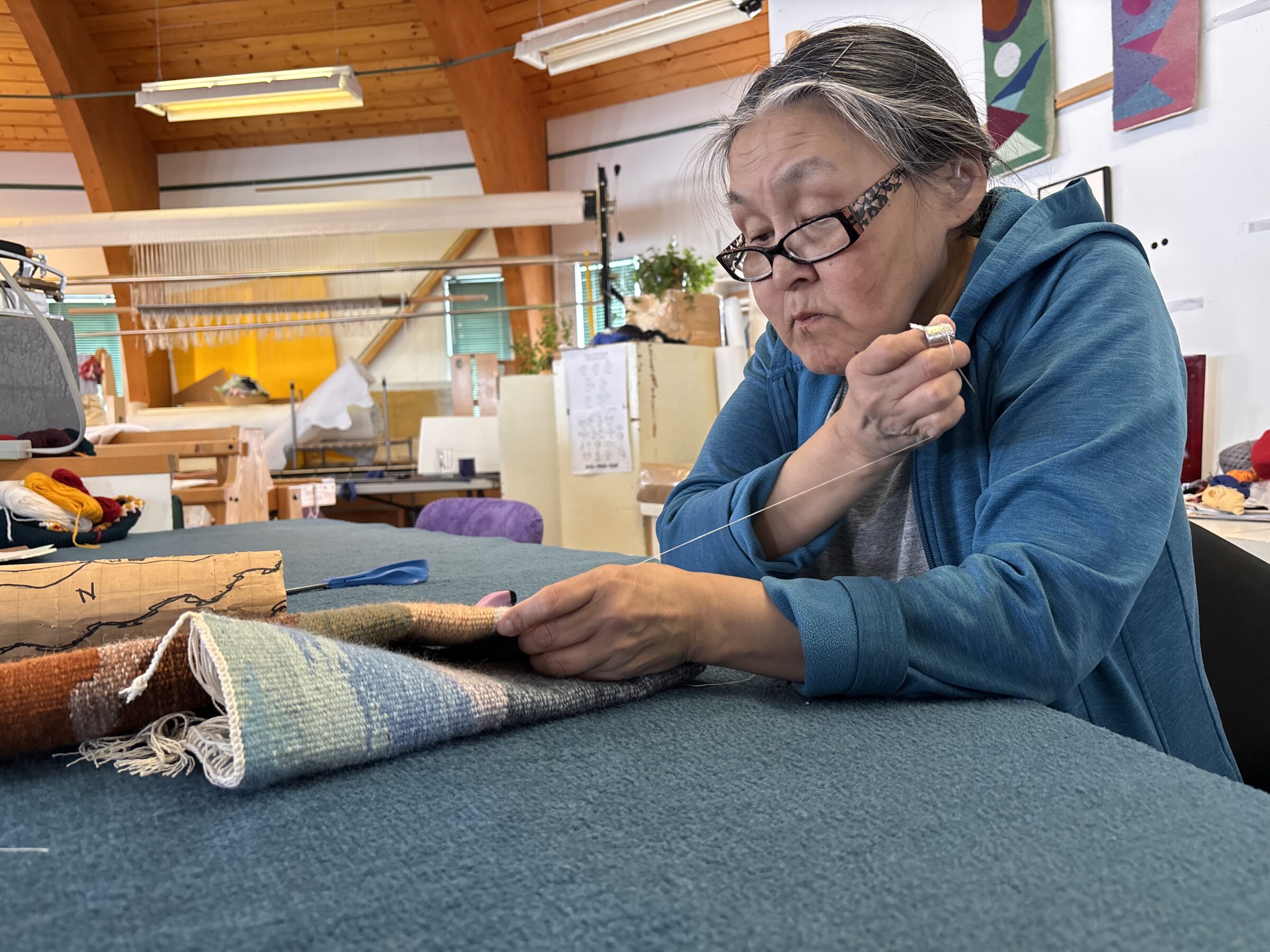 Paleah Kuniliusie sews a small tapestry last Friday at the Uqqurmiut Centre for Arts and Crafts in Pangnirtung. (Photo by Daron Letts)