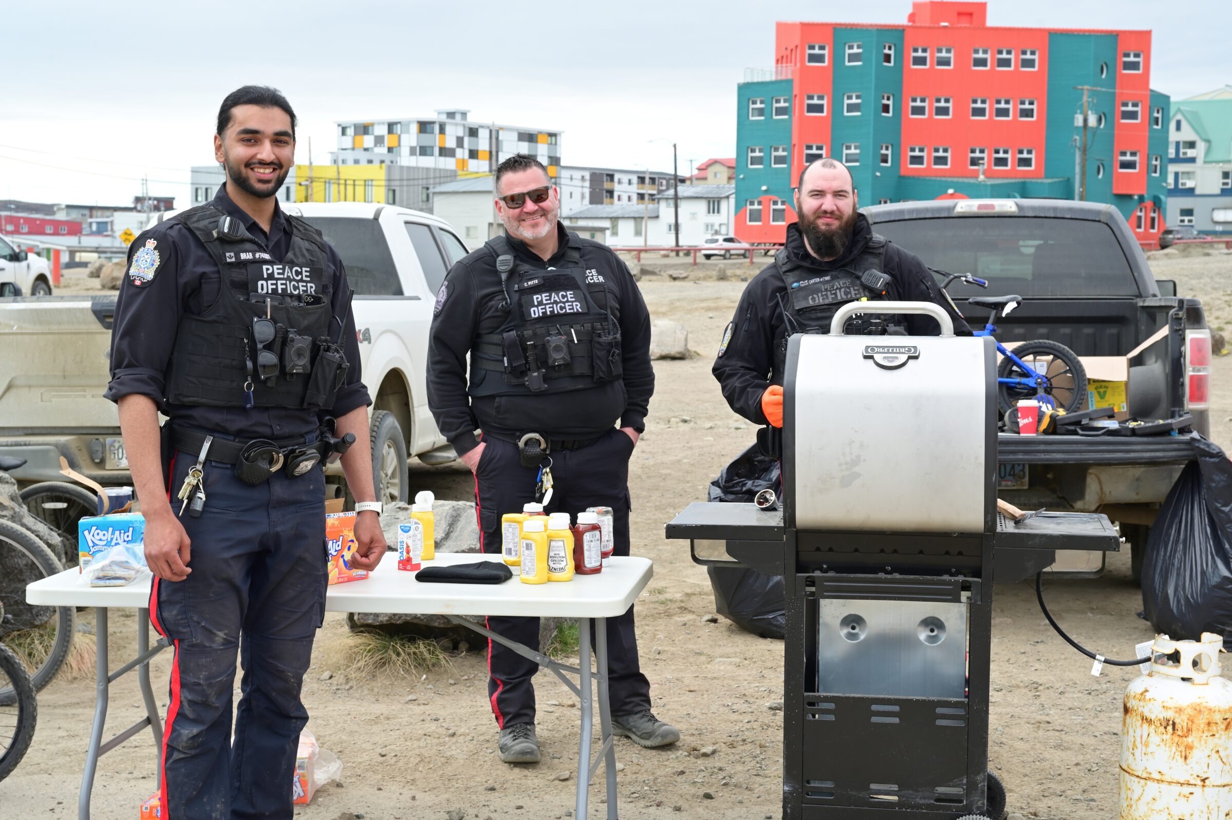 Municipal enforcement officers Daman Brar, left, Chris Pitts and Sgt. Harley Carter take part in an event Monday that teaches bike safety to kids. They also served up hot dogs at the basketball court in front of Nakasuk School. (Photo by Mosha Folger)