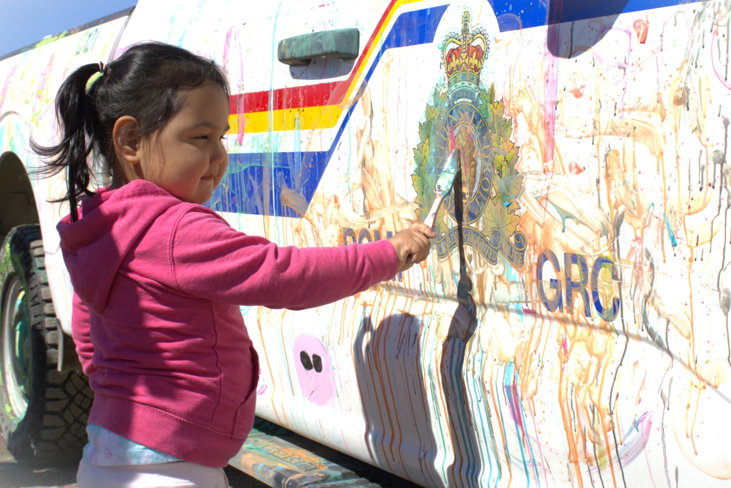 Sophie-Mae Panesar, 3, paints over the RCMP badge on a police truck Saturday as part of a children’s event hosted by officers at the Alianait Arts Festival in Iqaluit. The badge is inscribed with the motto, ‘maintiens le droit,’ or ‘uphold the right’ in English. (Photo by Daron Letts)